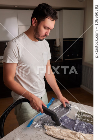 The girl pumps out air with a vacuum cleaner from a vacuum bag with clothes. The concept of storage and transportation of clothing, things. Space saving seal bag. The girl pumps out air with a vacuum cleaner from a vacuum bag with clothes. The concept of storage and transportation of clothing, things. Space saving seal bag. 106960592