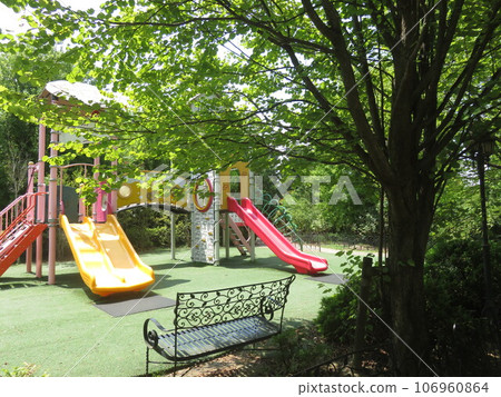 A slide in a playground surrounded by tree-shaded benches and greenery A slide in a playground surrounded by tree-shaded benches and greenery 106960864
