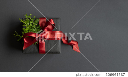 Black gift box with thuja and red ribbon on dark background. Flatly, copyspace. Black gift box with thuja and red ribbon on dark background. Flatly, copyspace. 106961387