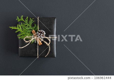 Black gift box with thuja and cinnamon on a dark background. Copyspace. 106961444
