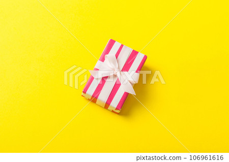 wrapped Christmas or other holiday handmade gift box in color paper with ribbon on colored background. Present box, decoration of gift on colored table, top view with copy space 106961616