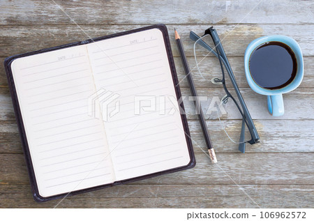 Blank paper notebook,glasses,pencil and cup of coffee on brown wooden table background. Blank paper notebook,glasses,pencil and cup of coffee on brown wooden table background. 106962572