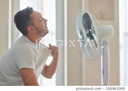 Young man relaxing under the air fan at home 106963060