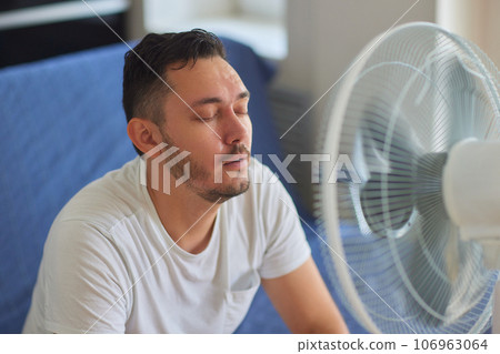 Young man relaxing under the air fan at home 106963064
