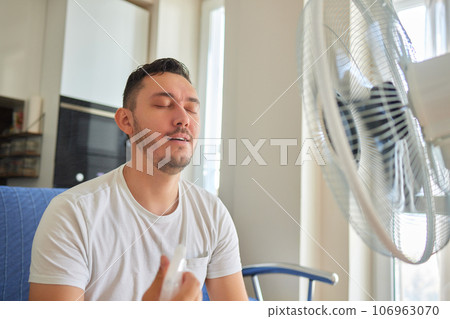 Young man relaxing under the air fan at home Young man relaxing under the air fan at home 106963070