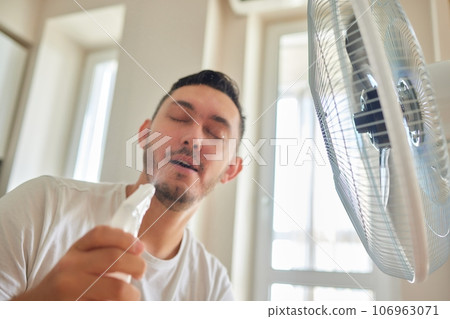Young man relaxing under the air fan at home Young man relaxing under the air fan at home 106963071