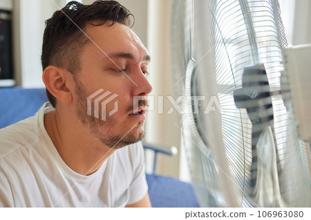 Young man relaxing under the air fan at home Young man relaxing under the air fan at home 106963080