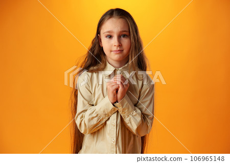 Little girl begging looking at viewer against yellow backgorund in studio Little girl begging looking at viewer against yellow backgorund in studio 106965148