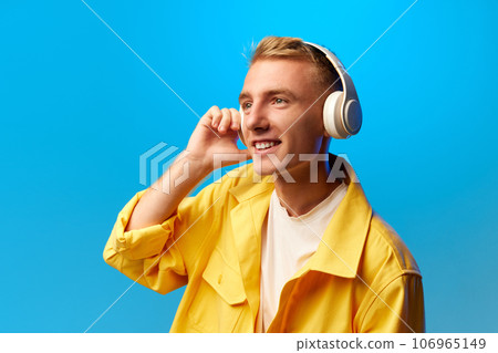 Portrait of young handsome smiling guy, student in bright fashion outfit and listening misic in headphones isolated on blue background. Portrait of young handsome smiling guy, student in bright fashion outfit and listening misic in headphones isolated on blue background. 106965149