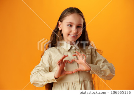Happy little girl making heart shape by hands on yellow background Happy little girl making heart shape by hands on yellow background 106965156