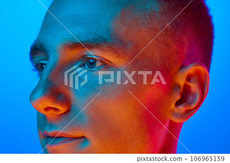 Close Up side view portrait of young handsome calm guy, student isolated on blue background in red neon light, filter. Confident, serious man. 106965159