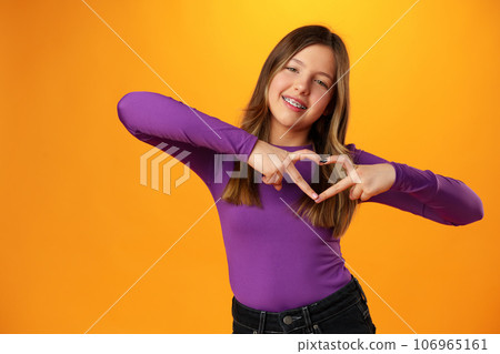 Friendly teen girl shows heart love gesture on yellow background Friendly teen girl shows heart love gesture on yellow background 106965161