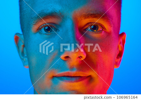 Close Up portrait of young handsome calm guy, student isolated on blue background in red neon light, filter. Confident, serious man. 106965164