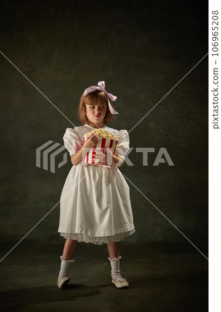 Portrait of disgruntled, unhappy girl standing with bucket of popcorn over vintage background. Fairy princess character of story tale. 106965208