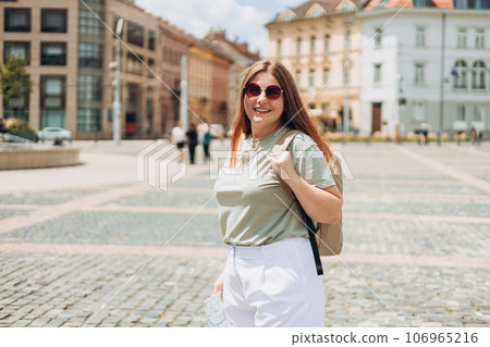 Sexy carefree woman posing on the street background. Positive model outdoors. Cheerful and happy girl in sunglasses with backpack walking on urban background, old town Sexy carefree woman posing on the street background. Positive model outdoors. Cheerful and happy girl in sunglasses with backpack walking on urban background, old town 106965216