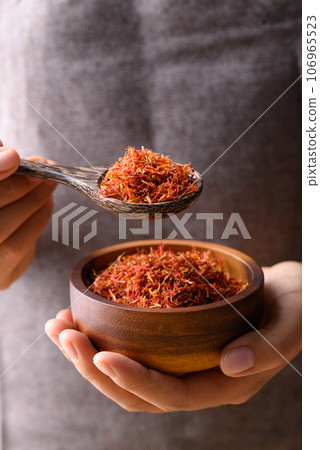 Dried safflower in wooden bowl and spoon holding by hand, Herbal tea 106965523
