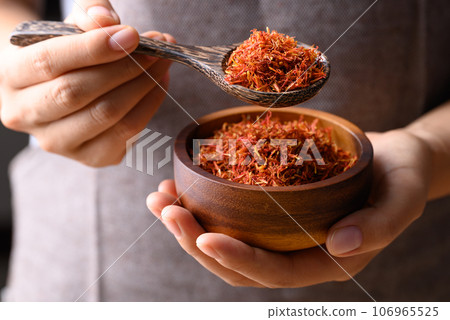 Dried safflower in wooden bowl and spoon holding by hand, Herbal tea 106965525