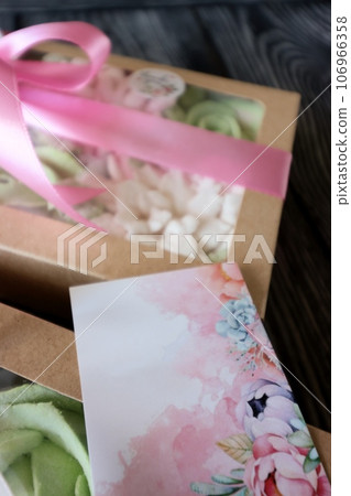 Two boxes with marshmallows. Zephyr flowers. Homemade marshmallows in a paper gift box. The box is tied with a ribbon tied into a bow. Label for the text. Near the congratulatory postcard. Close-up. Two boxes with marshmallows. Zephyr flowers. Homemade marshmallows in a paper gift box. The box is tied with a ribbon tied into a bow. Label for the text. Near the congratulatory postcard. Close-up. 106966358