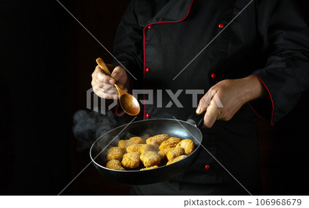 The cook prepares crispy nagits in a frying pan. Recipe for delicious food and dishes on a dark background. Free ad space The cook prepares crispy nagits in a frying pan. Recipe for delicious food and dishes on a dark background. Free ad space 106968679