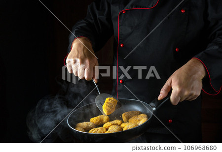 Cooking crispy chicken nuggets. The chef flips the nagits in a smoky hot pan. The idea of a large kitchen for a hotel with an advertising space Cooking crispy chicken nuggets. The chef flips the nagits in a smoky hot pan. The idea of a large kitchen for a hotel with an advertising space 106968680