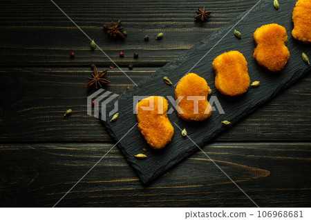 Crispy nuggets on a sorting board with spices. Fast food concept on dark background 106968681