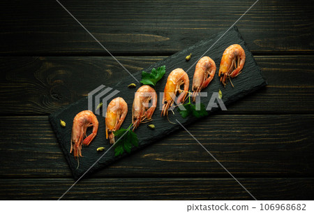 Boiled shrimp are laid out on a serving board with parsley and spices. The concept of table setting in a hotel or restaurant for dinner Boiled shrimp are laid out on a serving board with parsley and spices. The concept of table setting in a hotel or restaurant for dinner 106968682