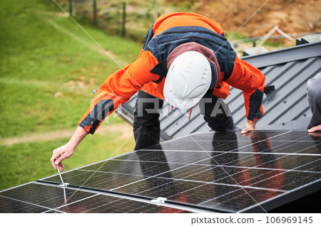 Builders installing photovoltaic solar panels on roof of house. Men engineers in helmets building solar module system with help of hex key. Concept of alternative, renewable energy. Builders installing photovoltaic solar panels on roof of house. Men engineers in helmets building solar module system with help of hex key. Concept of alternative, renewable energy. 106969145