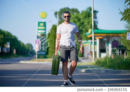 Confident man finally found petrol station and fill canister. Man returning to car to refuel it. Young male with canister in hand on background of gas station. Confident man finally found petrol station and fill canister. Man returning to car to refuel it. Young male with canister in hand on background of gas station. 106969150
