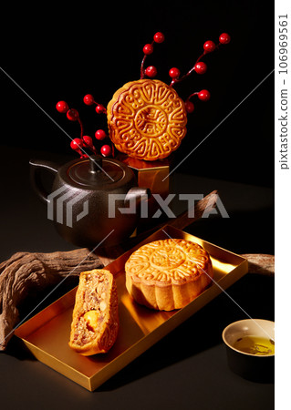 Festival mooncakes arranged on a golden dish, decorated with tree branch and a tea set. Black background. Tasty round moon cakes at mid autumn festival 106969561