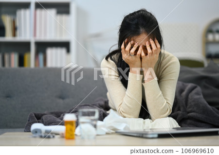 Sad lonely young woman having psychological trouble sitting in living room with prescription pill bottles. Mental heath concept Sad lonely young woman having psychological trouble sitting in living room with prescription pill bottles. Mental heath concept 106969610