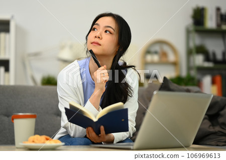 Thoughtful young female freelancer thinking, solving problem and using laptop in living room Thoughtful young female freelancer thinking, solving problem and using laptop in living room 106969613