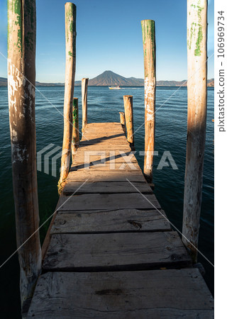 Wooden dock on Lake Atitlan on the beach in Panajachel, Guatemala. With Toliman and San Pedro volcanoes in the background 106969734