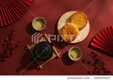 Advertising layout for moon cake products on a red background. Mooncakes on wooden tray decorated with set of tea and some pretties. Chinese Mid-Autumn Festival concept Advertising layout for moon cake products on a red background. Mooncakes on wooden tray decorated with set of tea and some pretties. Chinese Mid-Autumn Festival concept 106969920