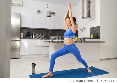 Portrait of young fitness instructor, woman doing yoga, standing in asana on rubber mat, workout at home 106969954
