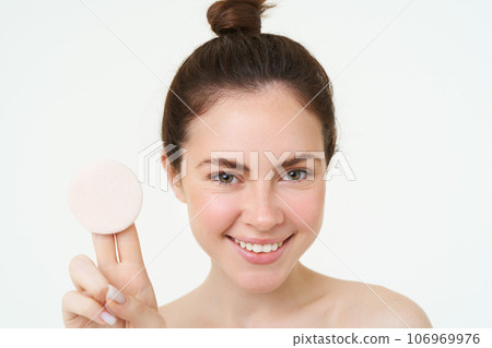 Skincare and wellbeing. Young woman shows cosmetic cotton pad, takes off her makeup, using facial cleanser, washing her face with skincare treatment, standing over white background 106969976