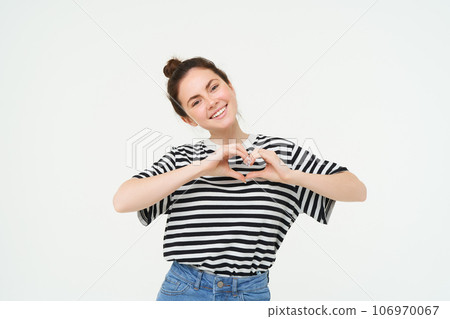 Beautiful european woman, shows heart sign, expresses her love and affection, flirting, standing over white background 106970067