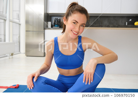 Yoga, welness and wellbeing. Young woman workout, does sport at home, female fitness instructor stretches before exercises on rubber mat in living room Yoga, welness and wellbeing. Young woman workout, does sport at home, female fitness instructor stretches before exercises on rubber mat in living room 106970150