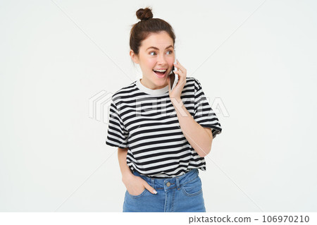Portrait of enthusiastic young woman talking on mobile phone, chatting with friend, reacts to surprising news received by telephone, white background 106970210