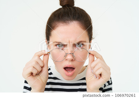 Close up of shocked, insulted young woman, frowning and looking offended, reading smth offensive and upsetting, takes off glasses, stands over white background Close up of shocked, insulted young woman, frowning and looking offended, reading smth offensive and upsetting, takes off glasses, stands over white background 106970261