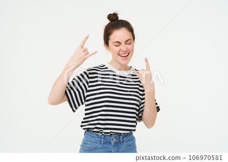 Portrait of attractive, carefree woman dancing, showing heavy metal, rock on gesture, standing over white background 106970581