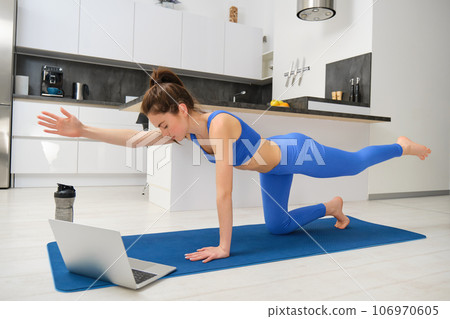 Portrait of woman doing stretching exercises, follows tutorial on laptop, attends online yoga class from home, workout on rubber mat Portrait of woman doing stretching exercises, follows tutorial on laptop, attends online yoga class from home, workout on rubber mat 106970605