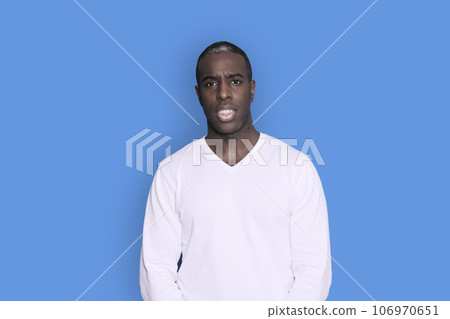 Portrait of cheerful young african-american guy wearing white casual sweater posing isolated on blue background Portrait of cheerful young african-american guy wearing white casual sweater posing isolated on blue background 106970651