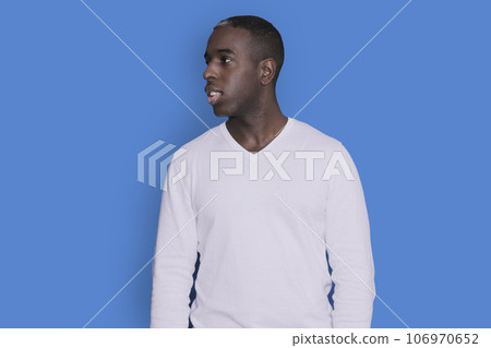 Portrait of cheerful young african-american guy wearing white casual sweater posing isolated on blue background. Carefree young millennial man aside Portrait of cheerful young african-american guy wearing white casual sweater posing isolated on blue background. Carefree young millennial man aside 106970652