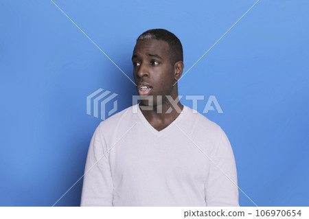 Portrait of cheerful young african-american guy wearing white casual sweater posing isolated on blue background. Carefree young millennial man aside Portrait of cheerful young african-american guy wearing white casual sweater posing isolated on blue background. Carefree young millennial man aside 106970654