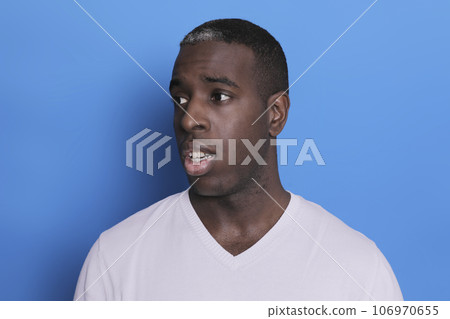 Portrait of cheerful young african-american guy wearing white casual sweater posing isolated on blue background. Carefree young millennial man aside Portrait of cheerful young african-american guy wearing white casual sweater posing isolated on blue background. Carefree young millennial man aside 106970655