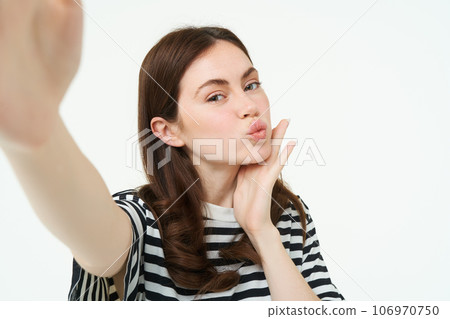 Portrait of cute, feminine girl posing near something, taking selfie on smartphone, holding camera with extended hand, isolated on white background 106970750