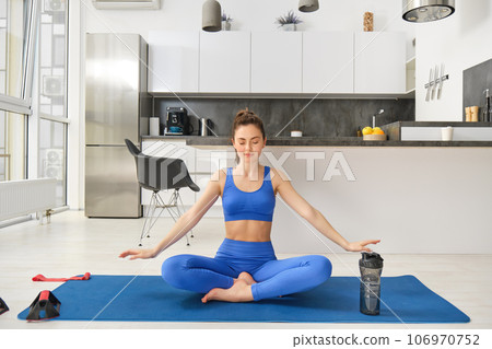 Portrait of calm and relaxed young woman, sitting on yoga rabber mat, concentrating on breathing exercises, doing mindful training at home Portrait of calm and relaxed young woman, sitting on yoga rabber mat, concentrating on breathing exercises, doing mindful training at home 106970752