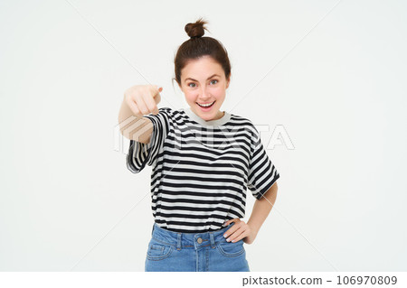 Image of confident, happy young woman in casual clothes, pointing finger at camera, laughing and smiling, standing over white background Image of confident, happy young woman in casual clothes, pointing finger at camera, laughing and smiling, standing over white background 106970809