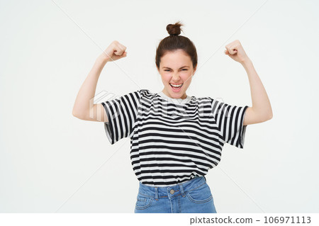 Image of sassy, strong and confident woman shows her muscles, flexing biceps, raising her arms high, standing over white background 106971113