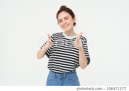 Portrait of cute girl, student shows thumbs up, recommends product, approves choice, likes item, stands over white background Portrait of cute girl, student shows thumbs up, recommends product, approves choice, likes item, stands over white background 106971177